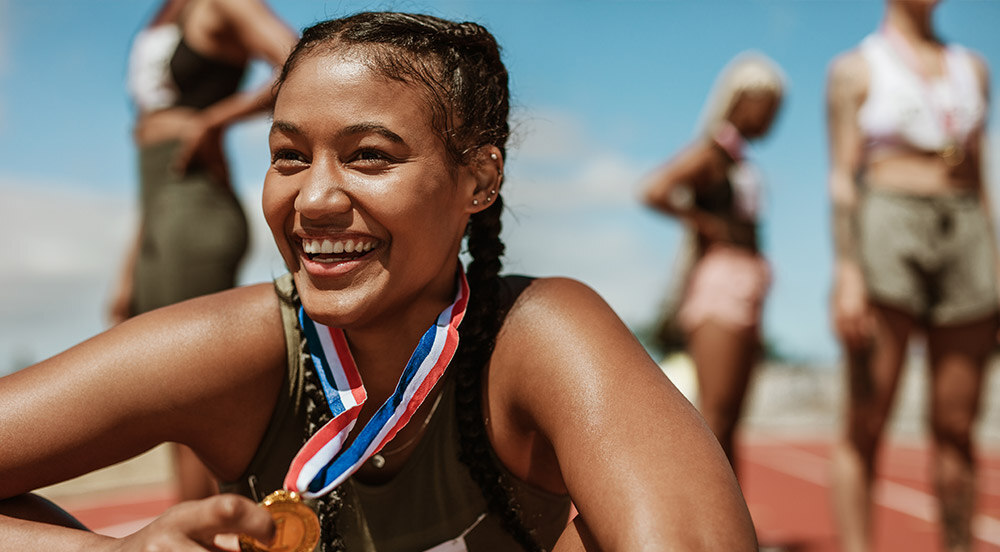 Atleta sorrindo com uma medalha no pescoço, pois ganhou a competição após fazer reposição hormonal feminina com Lybe Clinic.